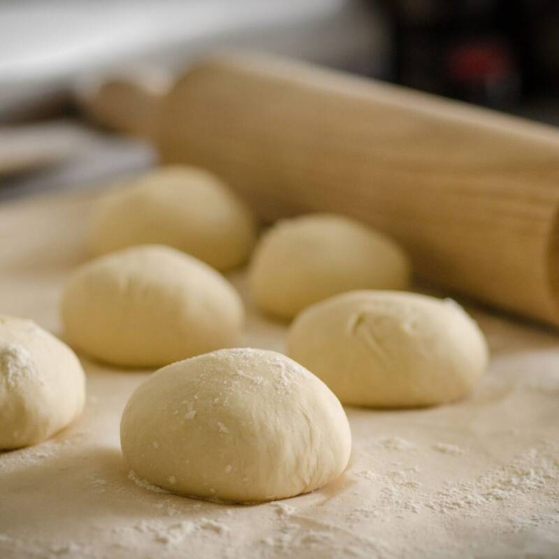 Homemade pizza dough balls resting on a floured counter with a wooden rolling pin