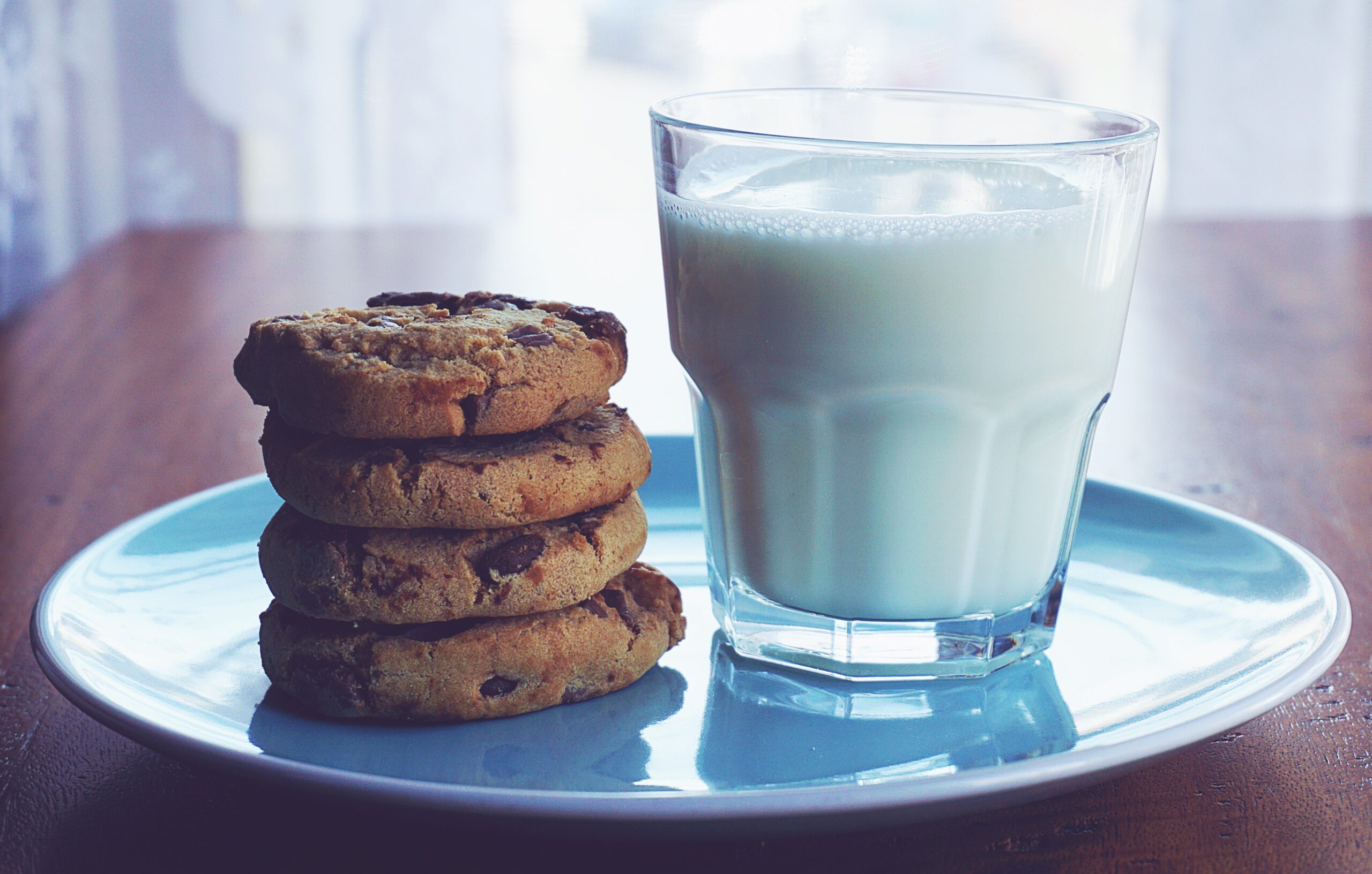 Baked classic chocolate chip cookies stacked next to a glass of milk