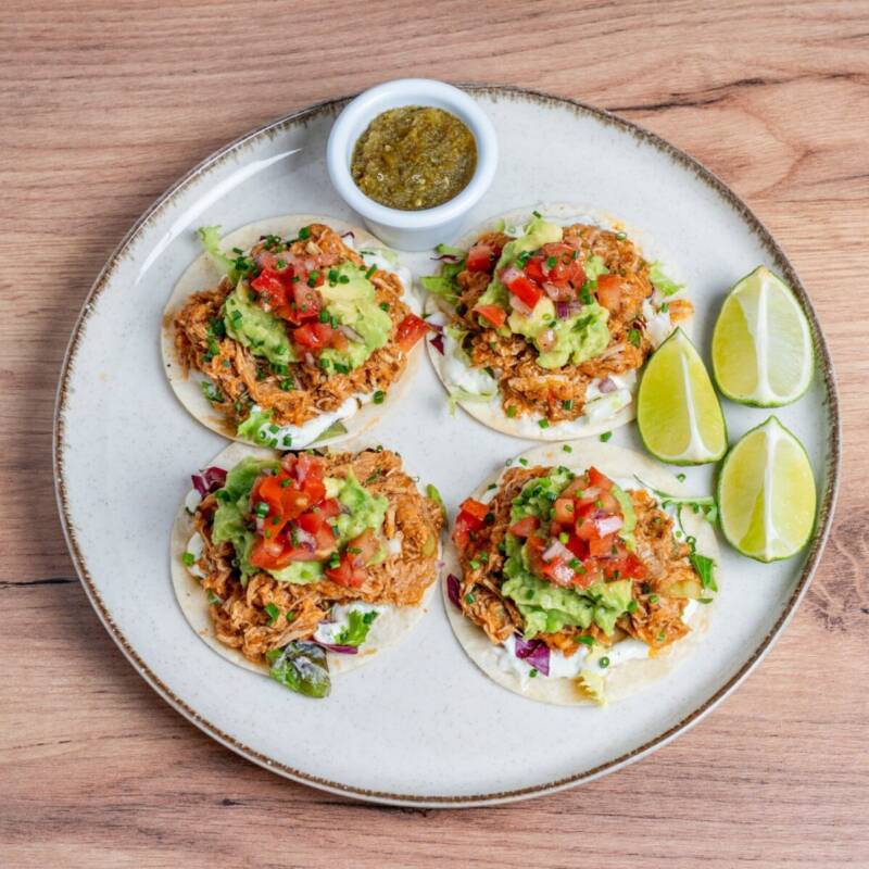 Tacos filled with shredded slow cooker BBQ chicken, guacamole, and lime