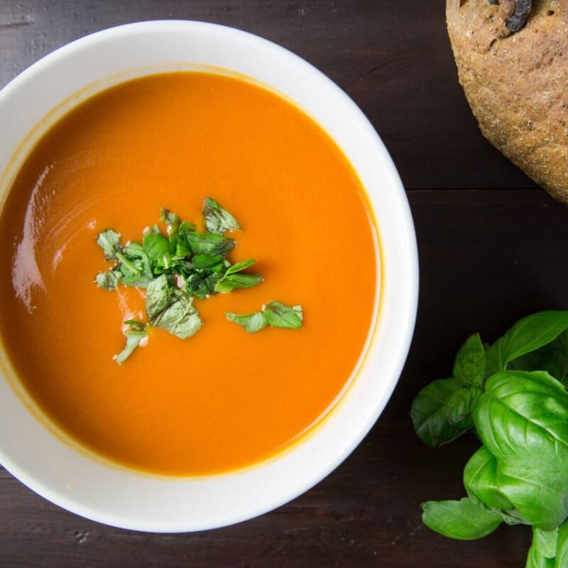 Bowl of creamy tomato basil soup garnished with fresh basil leaves and served with rustic bread